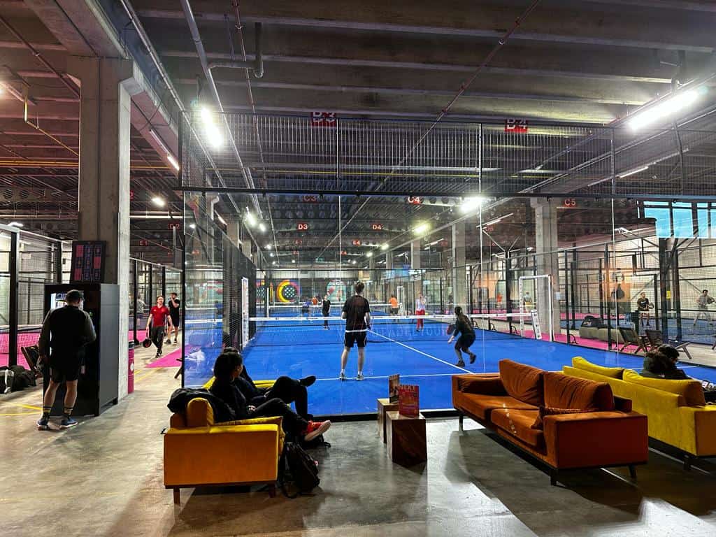 Two people playing padel netherlands on a blue court with couches