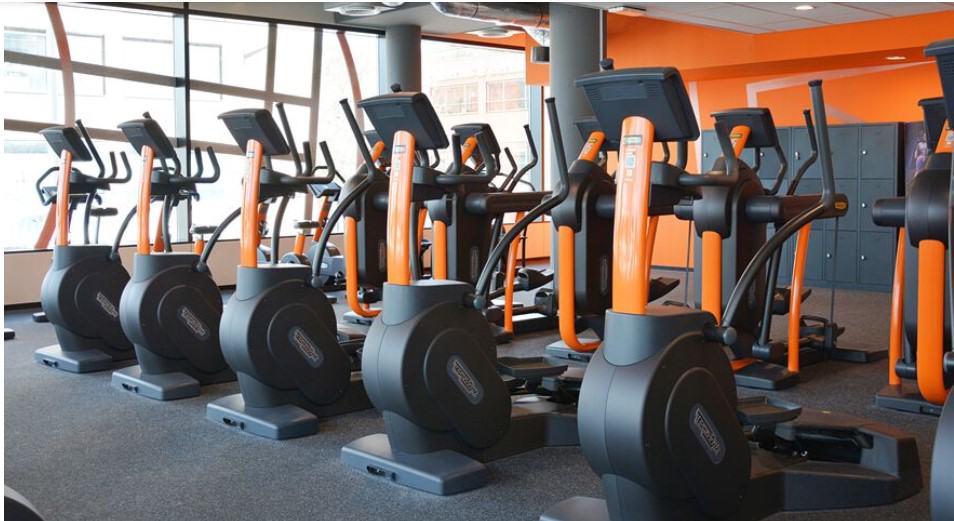 series of treadmills and ellipticals with an orange background