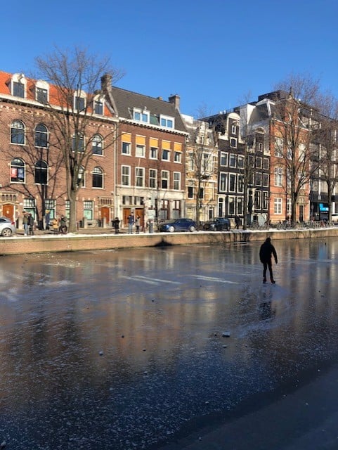 person skating on a canal with buildings on the background
