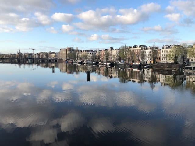 Amsterdam Canal Houses on the Amstel River with Blue sky and clouds reflected in the water