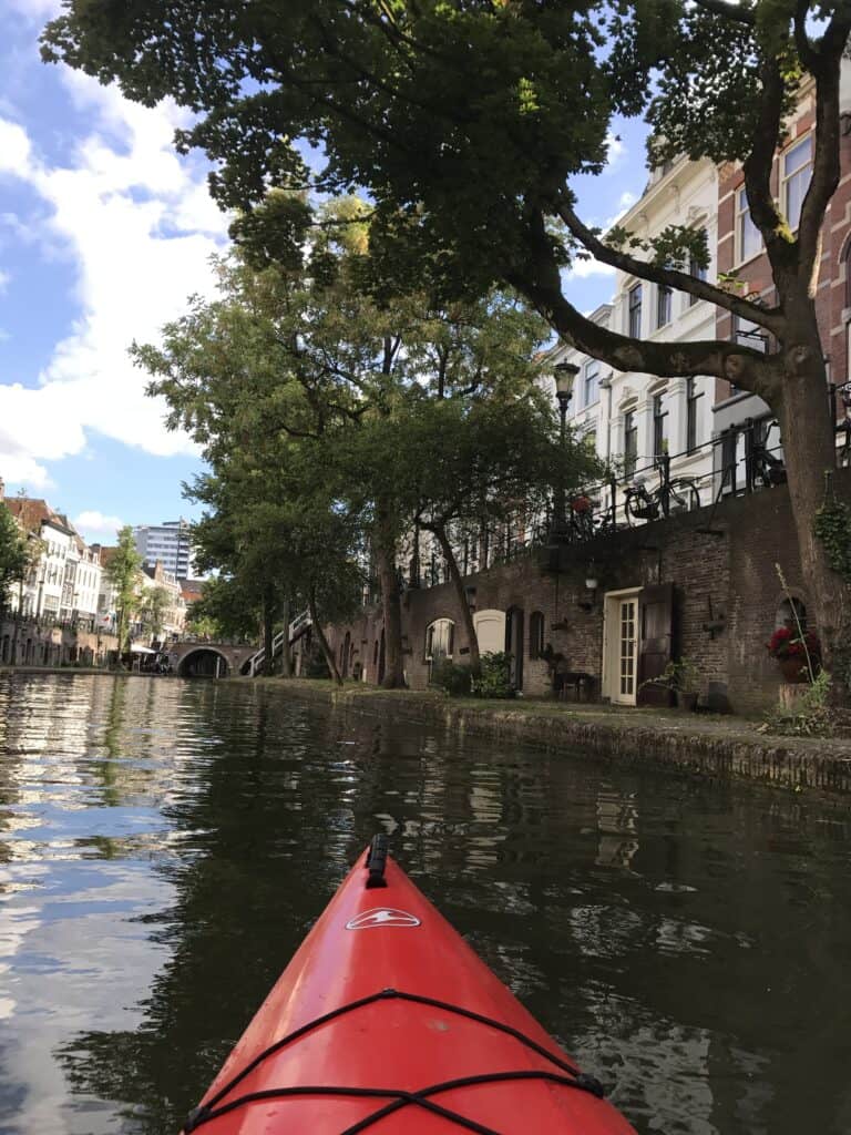 View from a red kayak paddling along the Utrecht canal past wharf-level cellars and terraces