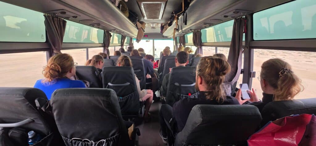 Inside the G Adventures Lando overland truck on a drive day, rows of passengers in their seats looking out at the desert through the windows